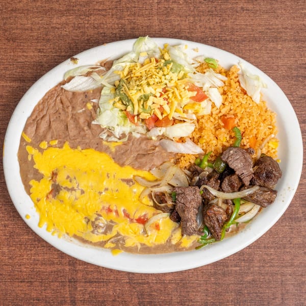 A white oval plate holds a Mexican dish with refried beans, rice, steak, and salad.