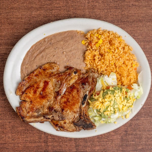 Two grilled pork chops with refried beans, rice, and a side salad with guacamole and cheese.