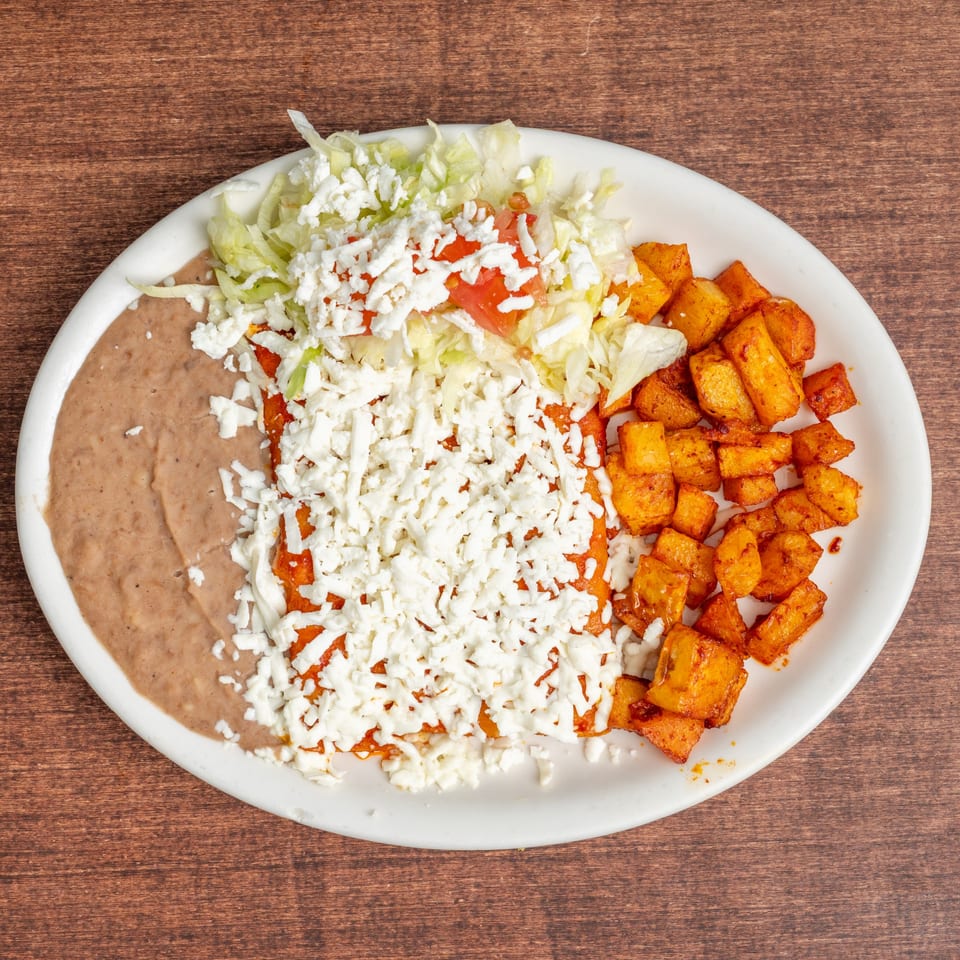 A plate of enchiladas topped with shredded lettuce, tomatoes, and cheese, served with refried beans and seasoned potatoes.