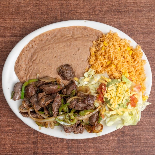 A white plate with steak fajitas, refried beans, Mexican rice, and a side salad with guacamole.
